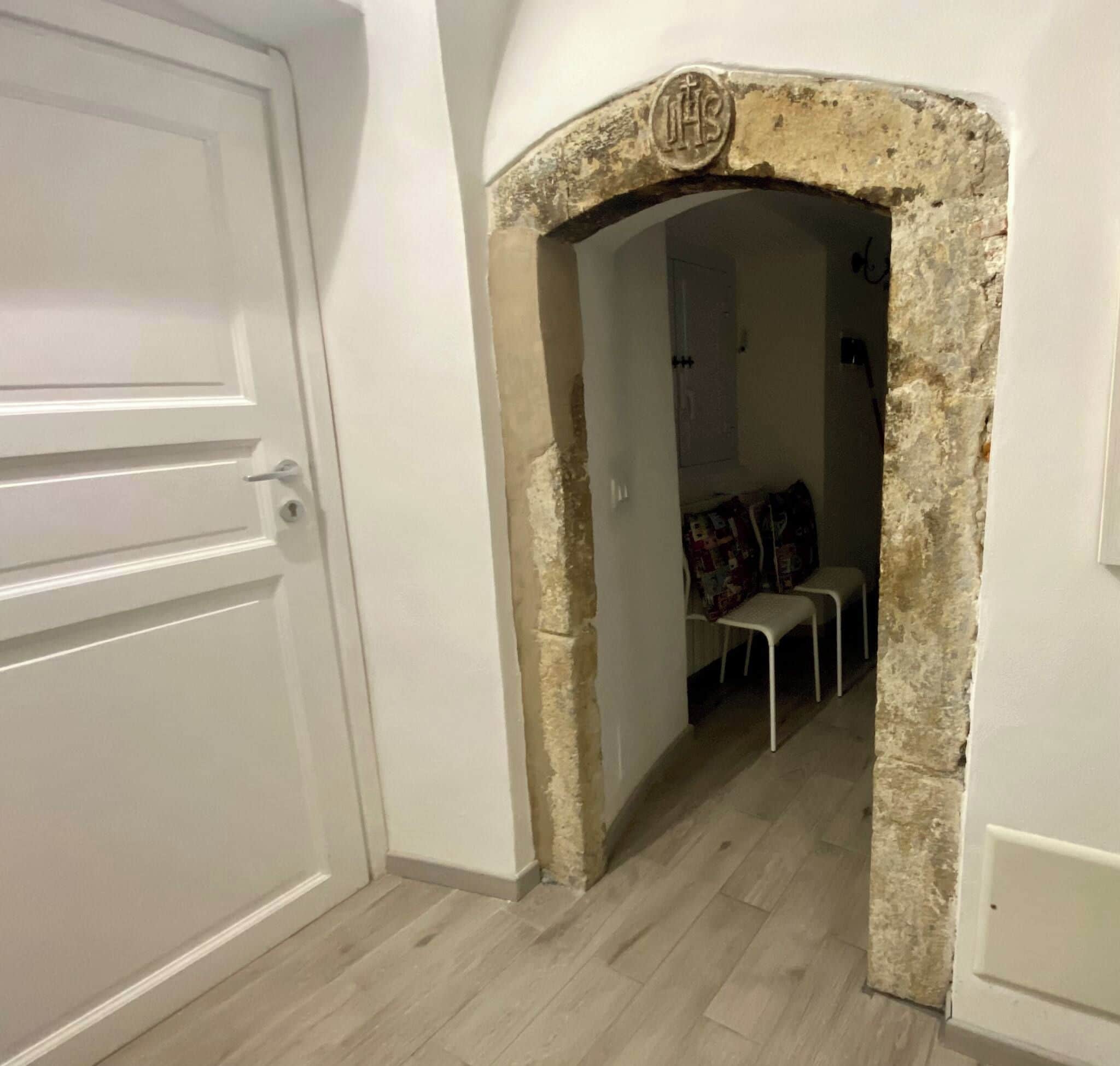 Un pasillo con una puerta blanca, un arco de piedra y una zona de estar con sillas y una mesa.