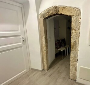 A hallway with a white door, a stone archway, and a seating area with chairs and a table. - IL Viaggiatore House (Calice Ligure)