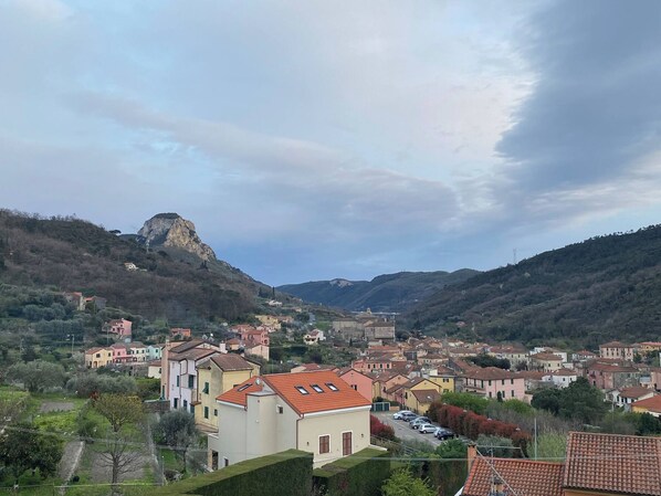 A hillside town with buildings, a prominent rock formation, and a clear sky. - IL Viaggiatore House (Calice Ligure)