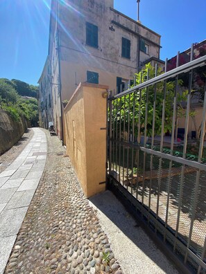 A narrow paved pathway flanked by a building with a beige facade and a metal gate. - IL Viaggiatore House (Calice Ligure)