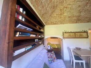 A cozy room with a wooden bookshelf, a white sofa, and a dining area. - IL Viaggiatore House (Calice Ligure)