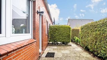 A red brick house with a white window and door, a small garden with a neatly trimmed hedge, and a clear blue sky.