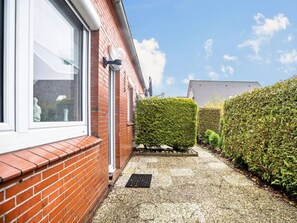 A red brick house with a white window and door, a small garden with a neatly trimmed hedge, and a clear blue sky. - Niedl App Helene 2 (Dornum)