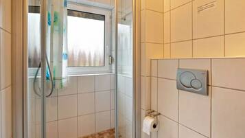 A bathroom with a shower, a toilet, and a window.