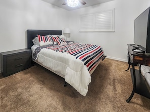 Un dormitorio con cama, mesitas de noche, lámpara, televisor y ventana con persianas.
