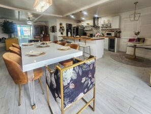 Una cocina moderna con una isla central, zona de comedor con sillas y un refrigerador visible.