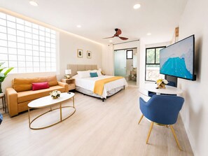 Una camera d'albergo moderna con un letto, un divano, un tavolino, una televisione e una ventola a soffitto.