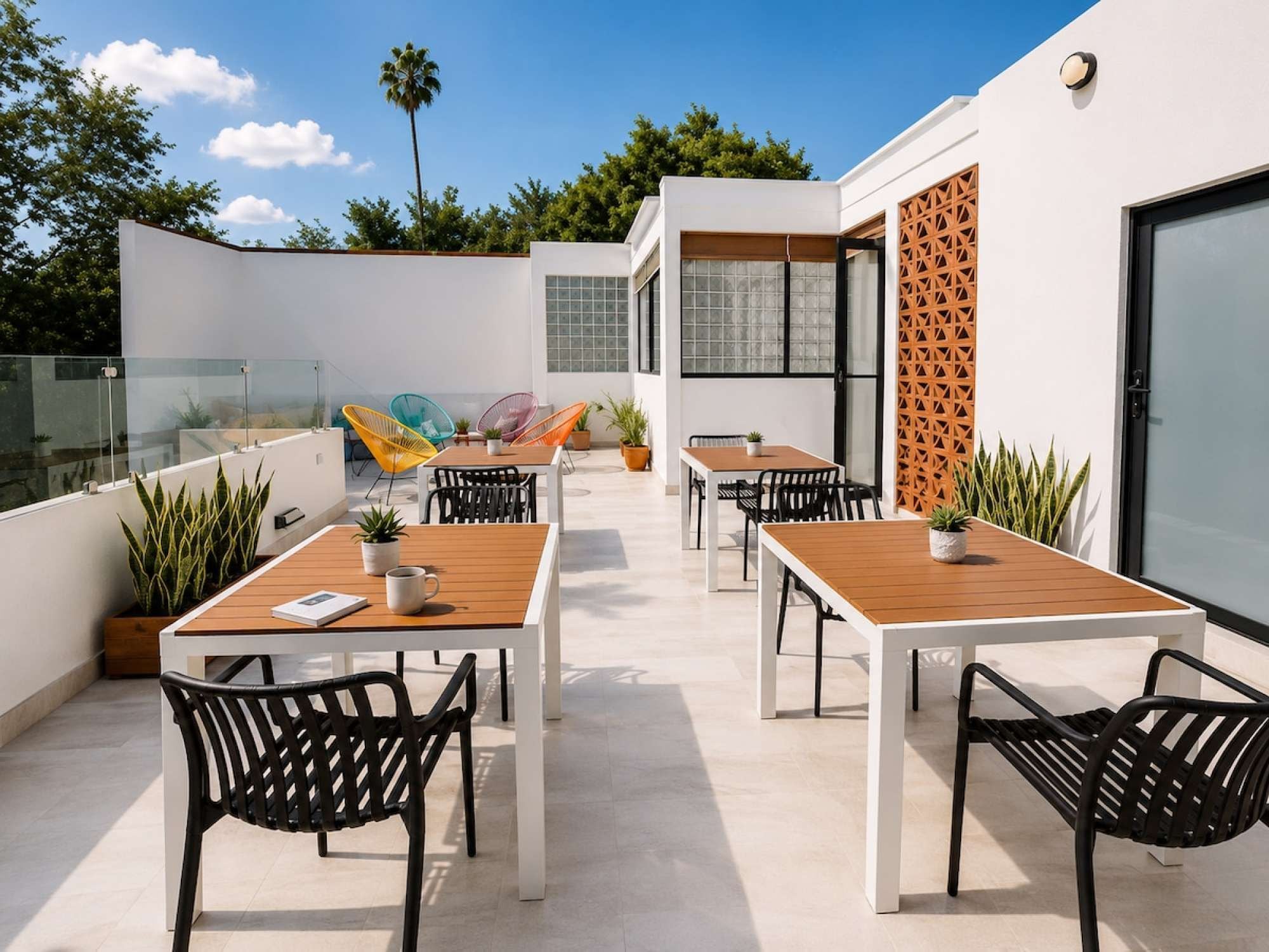 An outdoor patio with tables and chairs, potted plants, and a glass railing.