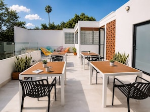 Patio esterno con tavoli e sedie, piante in vaso e ringhiera in vetro.