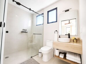 Un bagno moderno con doccia vetrata, un water, un lavandino con specchio sopra e una piccola finestra.