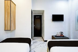Habitación de hotel con dos camas, televisión, armario y una mesita con hervidor y tazas.