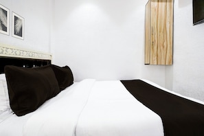Un lit bien fait, avec une literie blanche et noire, une tête de lit ornée de motifs décoratifs et une armoire en bois adossée à un mur blanc.