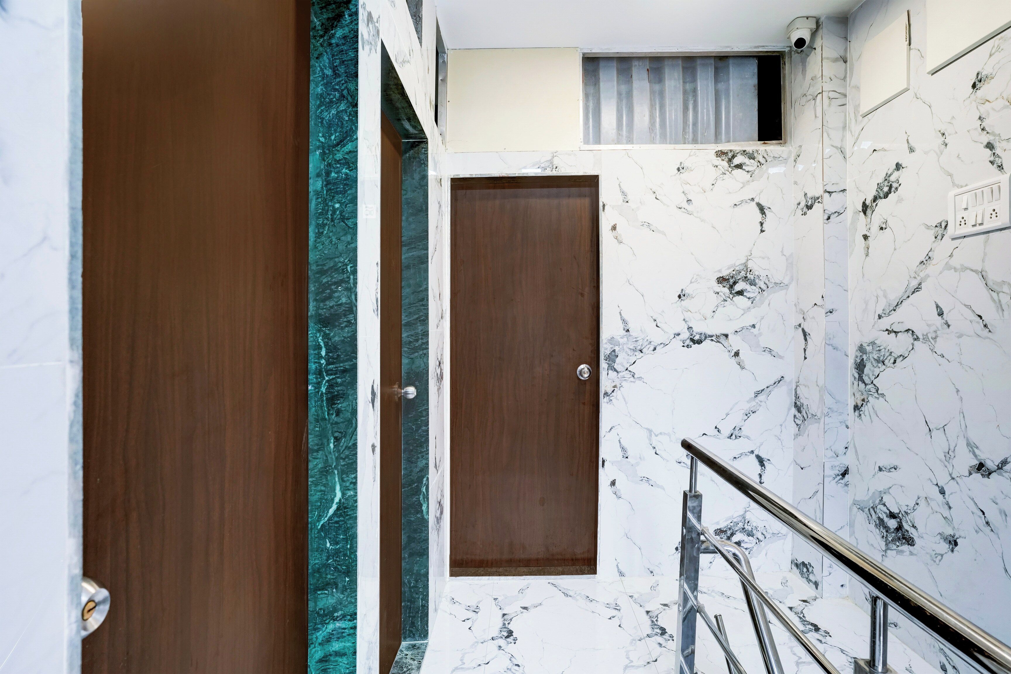 Una escalera de mármol con barandilla, una puerta de madera y un ventanal con cortina.