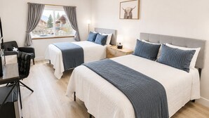 A hotel room with two beds, a desk, a chair, a window with curtains, and a framed picture on the wall.
