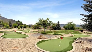 Un parcours de minigolf comportant plusieurs trous, entouré d’arbres et avec une chaîne de montagnes en arrière-plan.