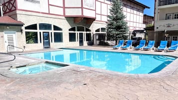 Une piscine avec une terrasse carrelée, une porte et un bâtiment à l’arrière-plan, doté d’une façade de style traditionnel.