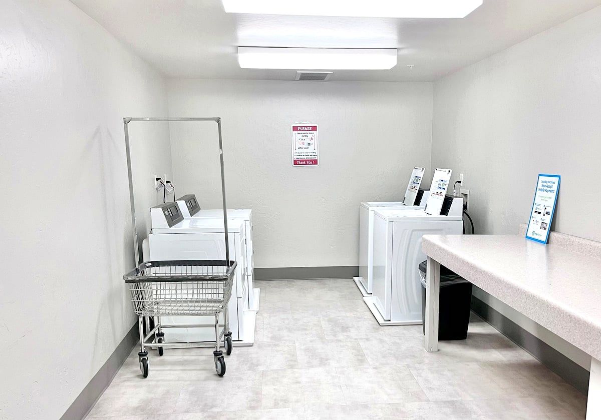 A laundry room with a cart, washing machines, and a sign on the wall.