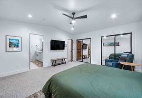 A bedroom with a bed, a TV, a bench, a mirror, and a door leading to another room.