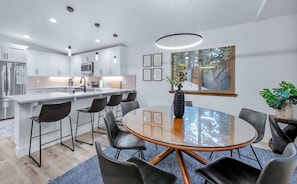 Una cocina moderna con gabinetes blancos, electrodomésticos de acero inoxidable y una isla central con taburetes de bar.