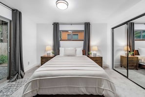 Un dormitorio con una cama grande, dos mesitas de noche con lámparas, una ventana con cortinas y un ventanal corredero.