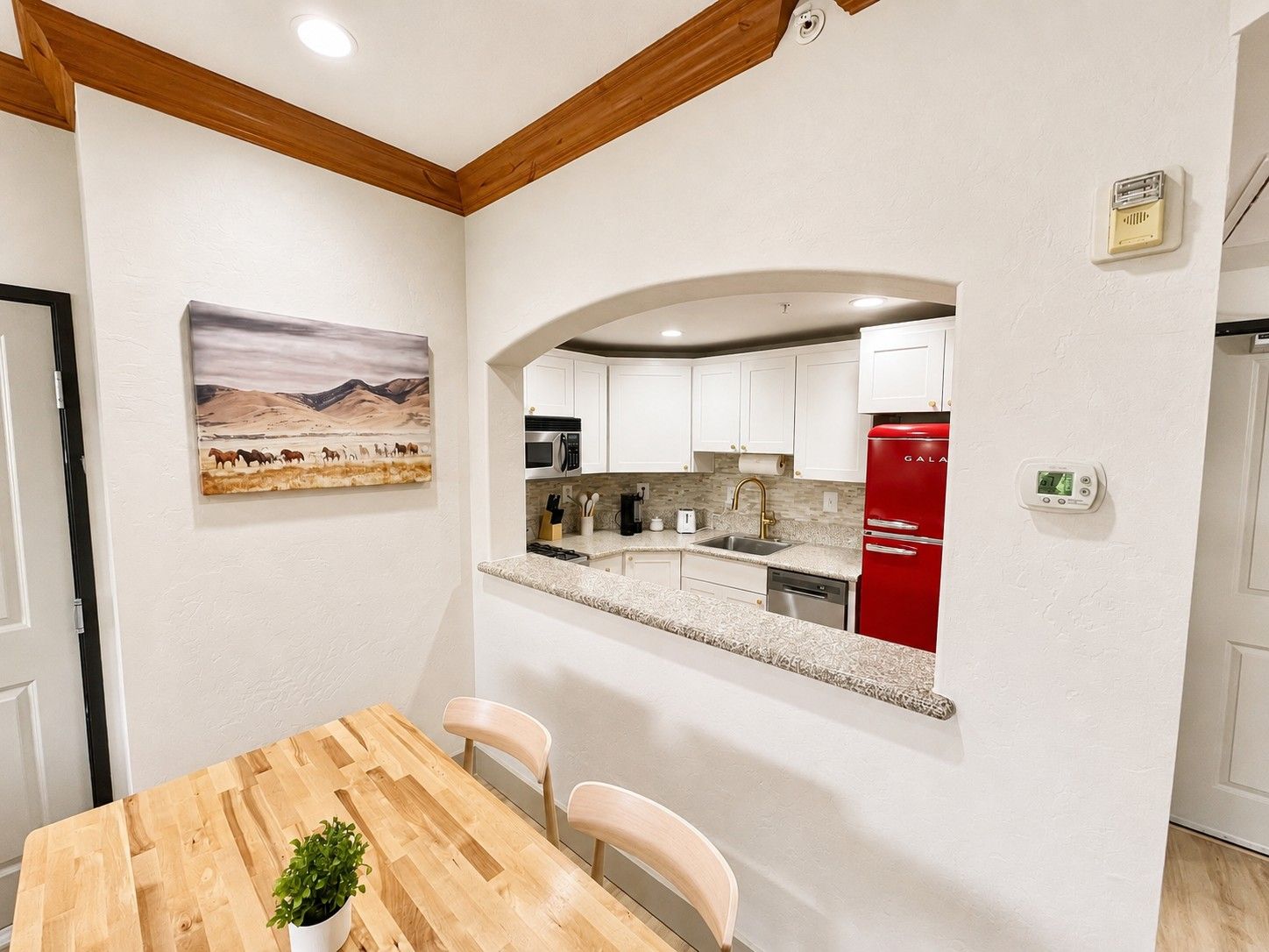 A modern kitchen with white cabinets, a red refrigerator, and a painting of a desert landscape.