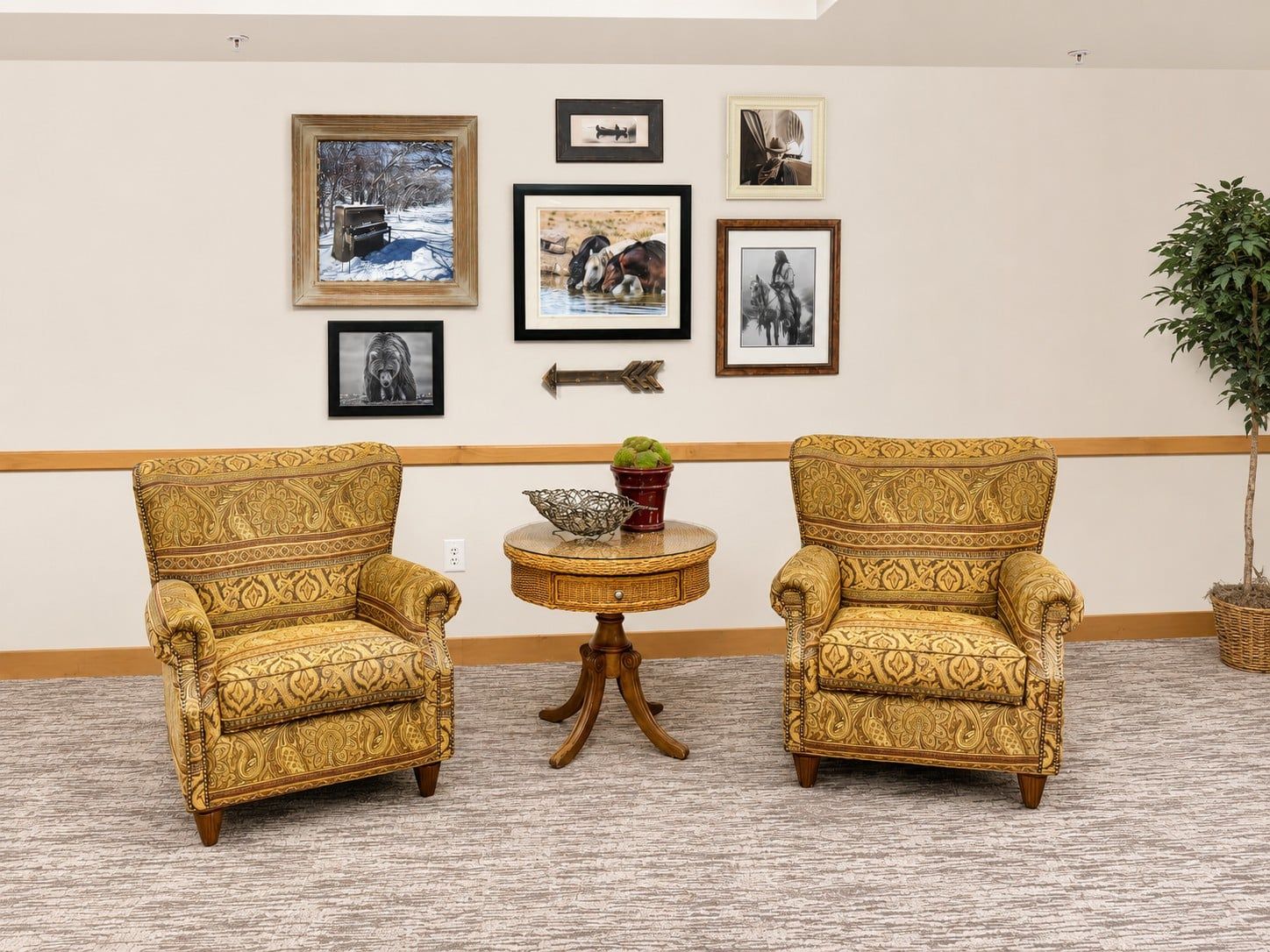 A room with two patterned armchairs, a small round table with a bowl and potted plant, and a wall decorated with framed pictures.