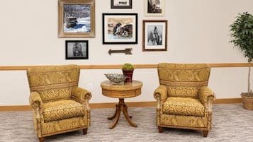 A room with two patterned armchairs, a small round table with a bowl and potted plant, and a wall decorated with framed pictures.