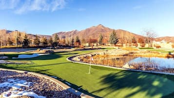 Un parcours de golf avec un étang, des arbres et des montagnes en arrière-plan.