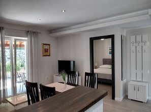 A modern interior with a dining area, a TV, and a bedroom visible through an open door. - Cozycorner (Konavle)