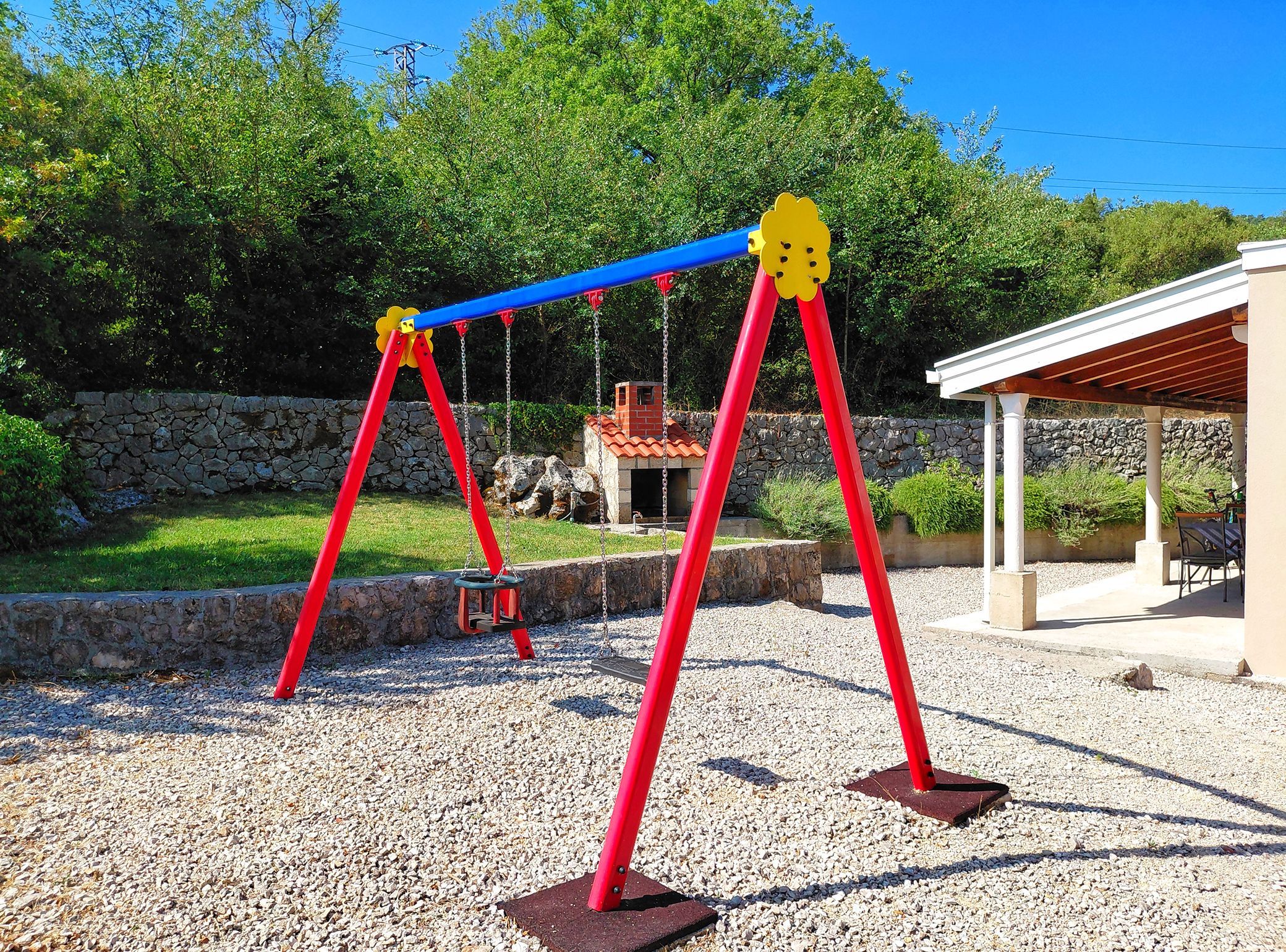 Une aire de jeux avec des balançoires, un mur en pierre et un pavillon abrité.