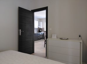 A room with a dark wooden door, a white dresser, and a view into a kitchen area with cabinets and appliances. - Cozycorner (Konavle)