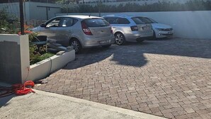 A parking area with three cars parked in a row, a paved walkway, and a building in the background. - Villa One (Jastrebarsko)