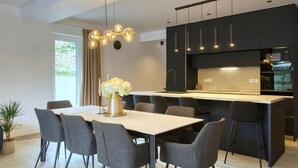 A modern kitchen with a central island, dark cabinetry, and a dining area with a table and chairs. - Villa One (Jastrebarsko)