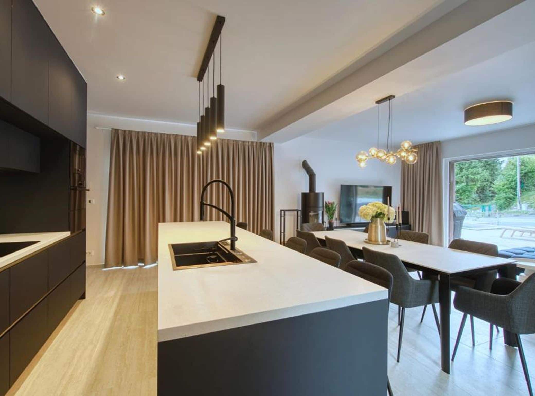 A modern kitchen with a central island, dark cabinetry, and a dining area with a large table and chairs.