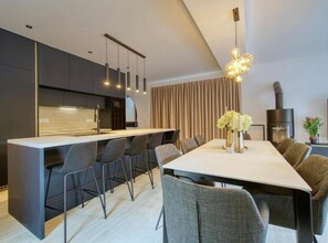 A modern kitchen with a central island, dining area with chairs, and a fireplace.