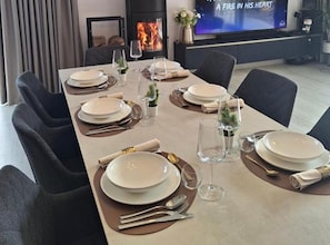 A dining table set with plates, cutlery, and glasses, with a fireplace in the background.