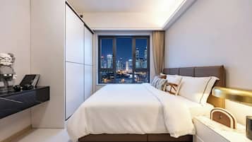Un dormitorio moderno con vista a la ciudad, una cama, una mesita de noche y un escritorio con una computadora y auriculares.