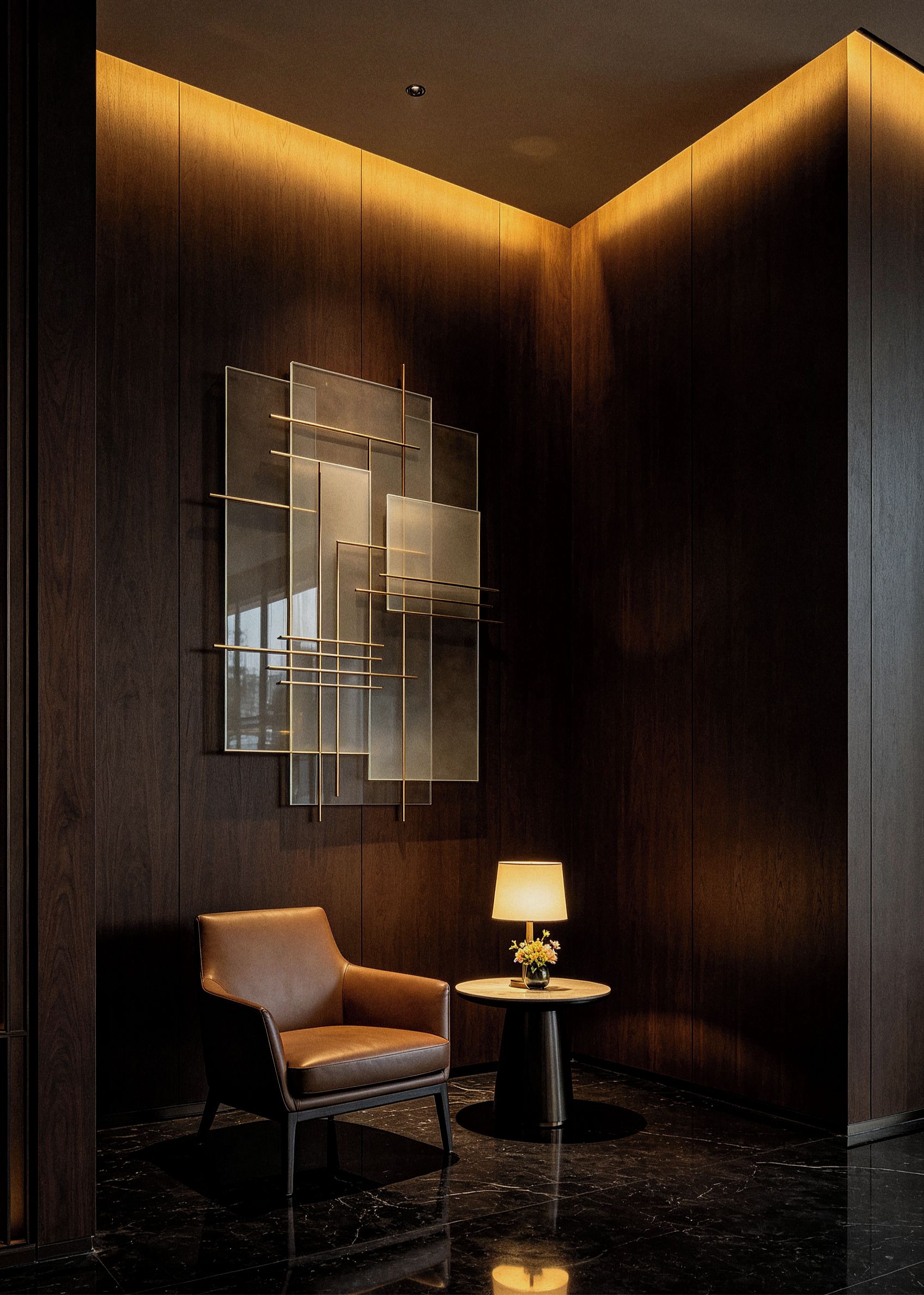 A modern interior with a dark wood panel wall, a geometric glass and metal art piece, a leather armchair, a small round table with a lamp, and a marble floor.