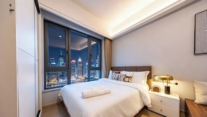 A modern hotel room with a large window offering a city view, a neatly made bed, a bedside table with a lamp, and a small wooden nightstand. - ruilantingyuan (shenzhen)