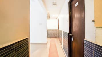 Een hotelgang met een houten deur, een betegelde vloer en een wandlamp.