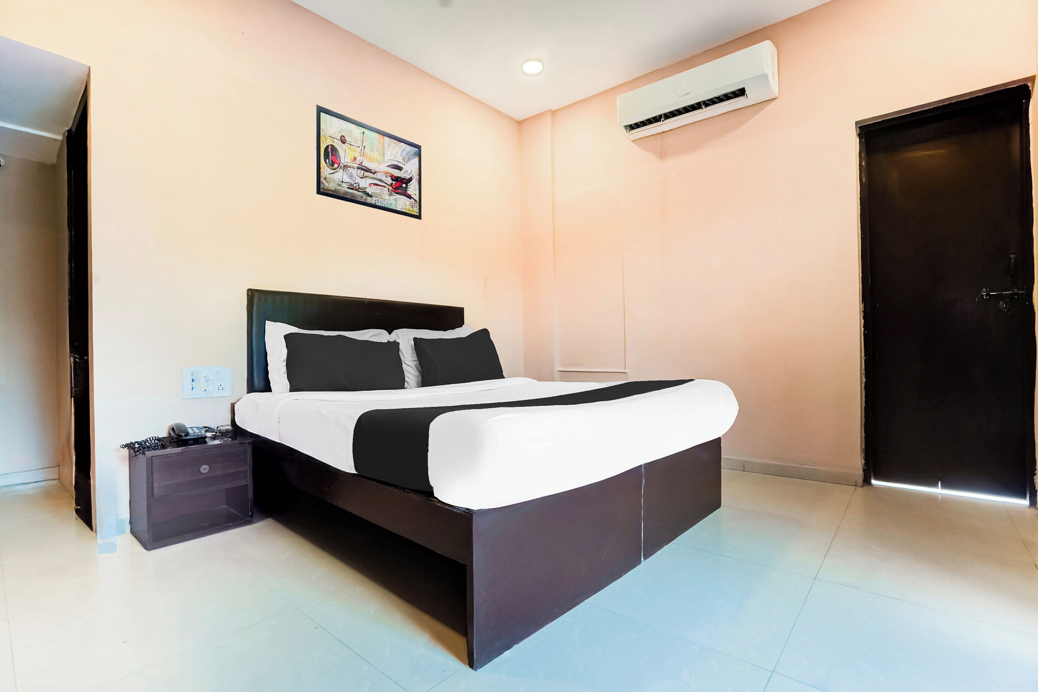A bedroom with a bed, a nightstand, a desk, an air conditioner, and a door.