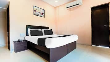 Een slaapkamer met een bed, nachtkastje, bureau, airconditioner en een deur.