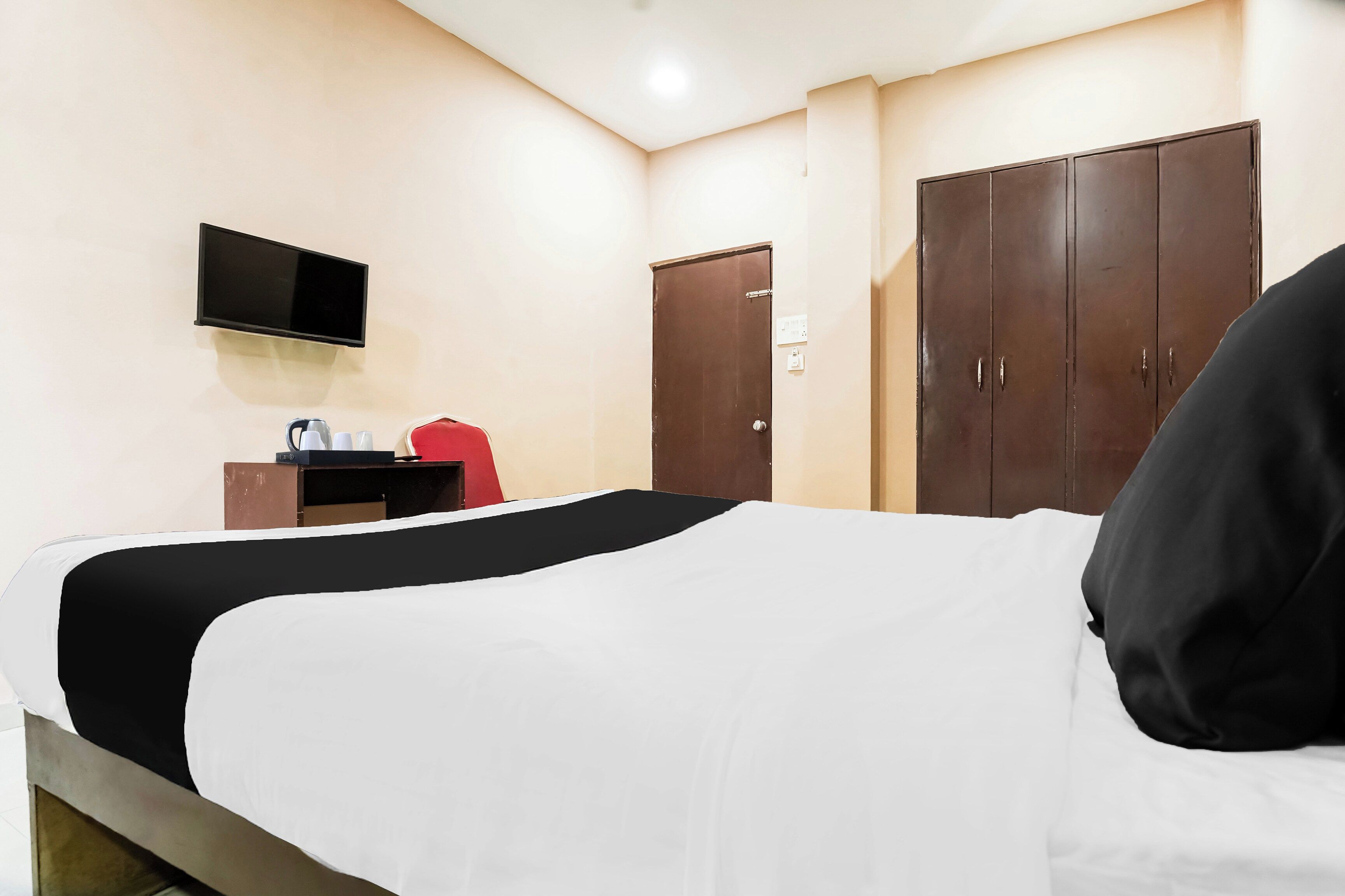 Una camera d'albergo con un letto, una televisione a parete, un armadio e una scrivania con una sedia rossa.