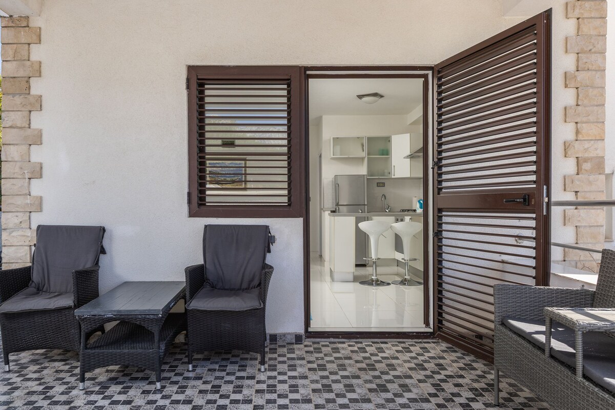 Ein Balkon mit Korbmöbeln, einem Schachbrettmuster Boden und Blick ins Badezimmer.