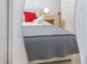 Ein ordentlich bezogenes Bett mit einer grauen Steude, einem roten Kopfkissen und einer Nachttischlampe.