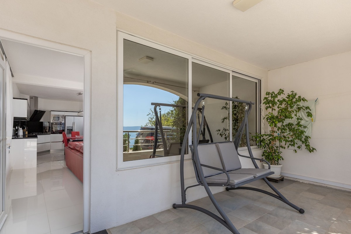 Ein Balkon mit Schaukelstuhl, Blumentopf und Blick auf das Meer.