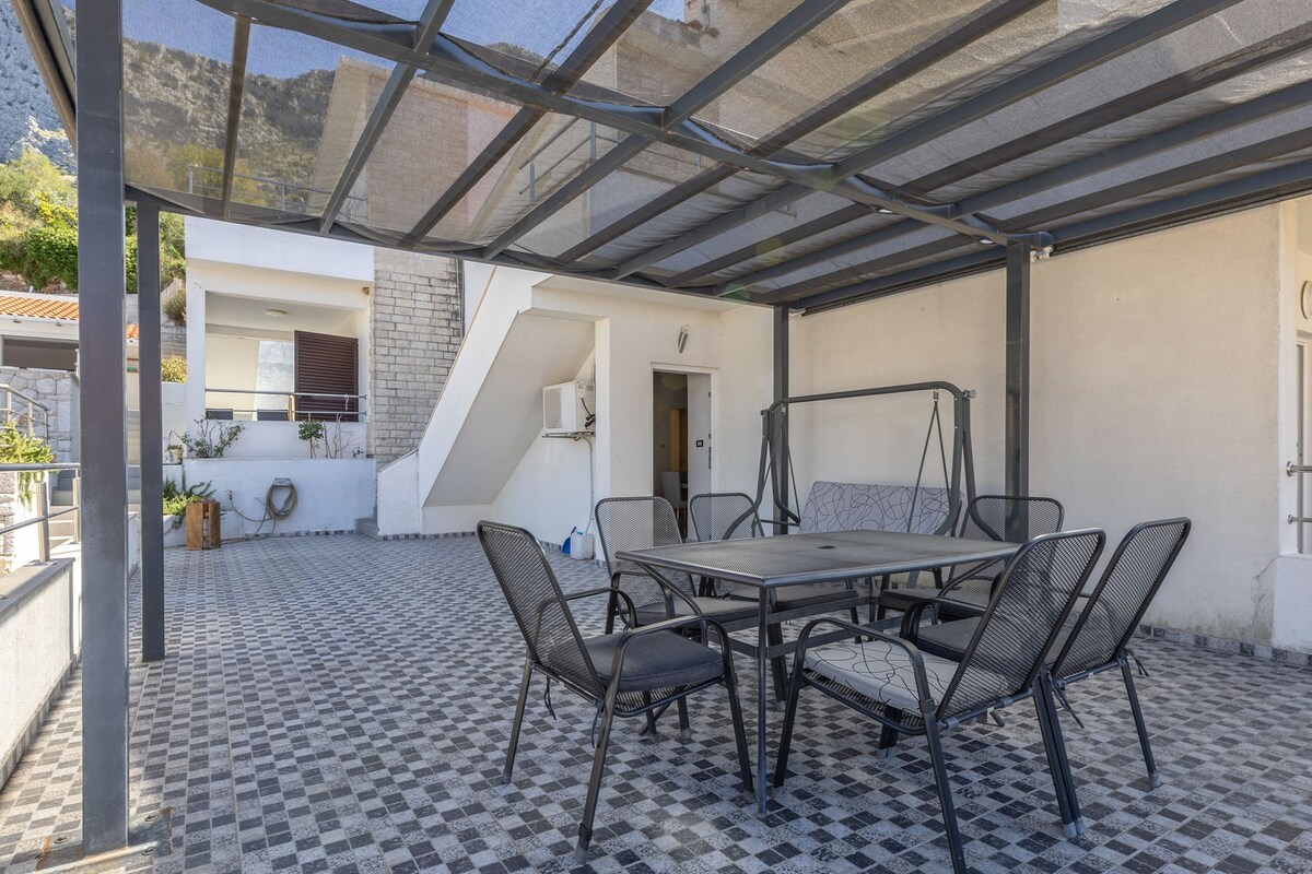 Eine Außenpatio mit Schachbrettboden, einem Tisch mit Stühlen und einem überdachten Bereich mit Blick auf die umliegende Landschaft.