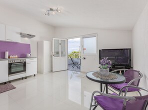 Una cucina moderna con forno, una zona pranzo con tavolo rotondo e sedie, e una televisione.