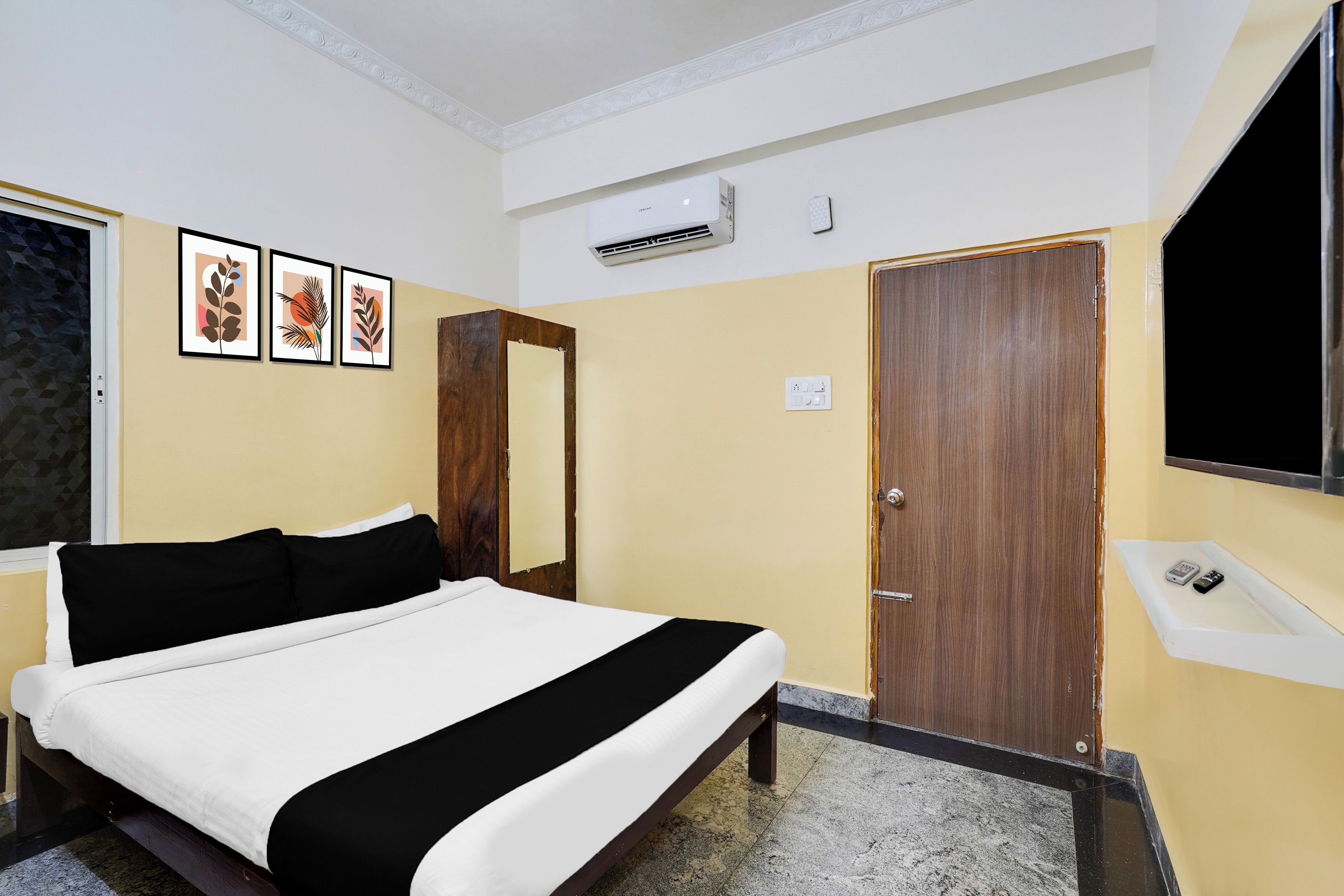 Una habitación de hotel con una cama, una puerta de madera, un equipo de aire acondicionado y un televisor instalado en la pared.