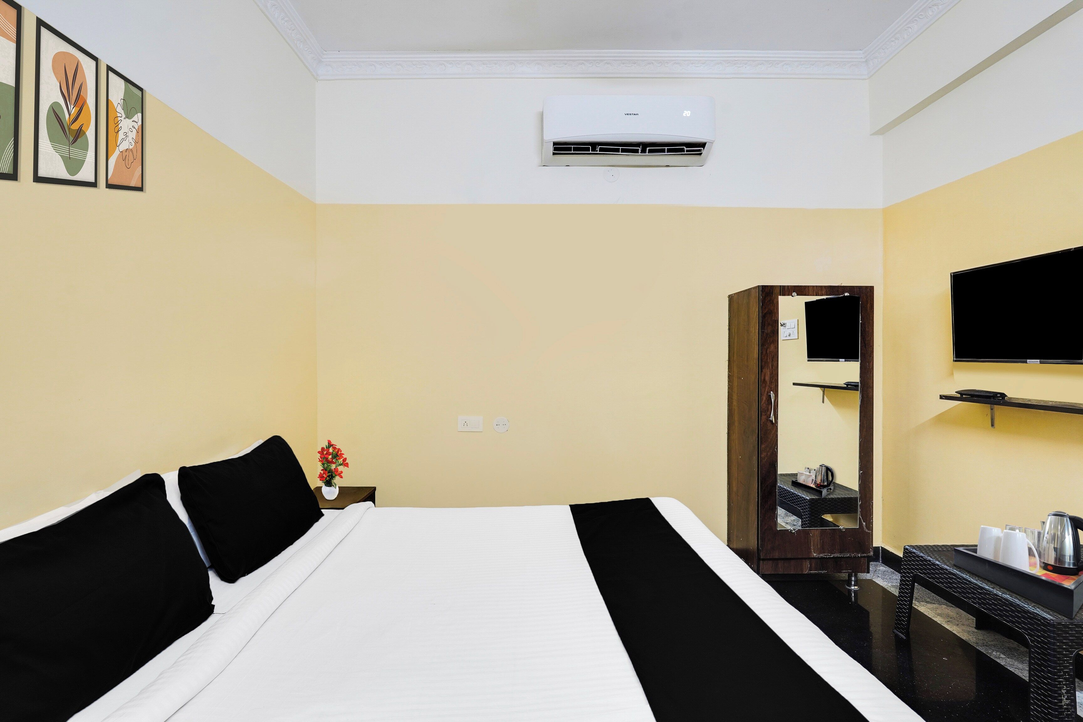Habitación de hotel con una cama, un televisor de pantalla plana montado en la pared, una mesita con un hervidor y un espejo.